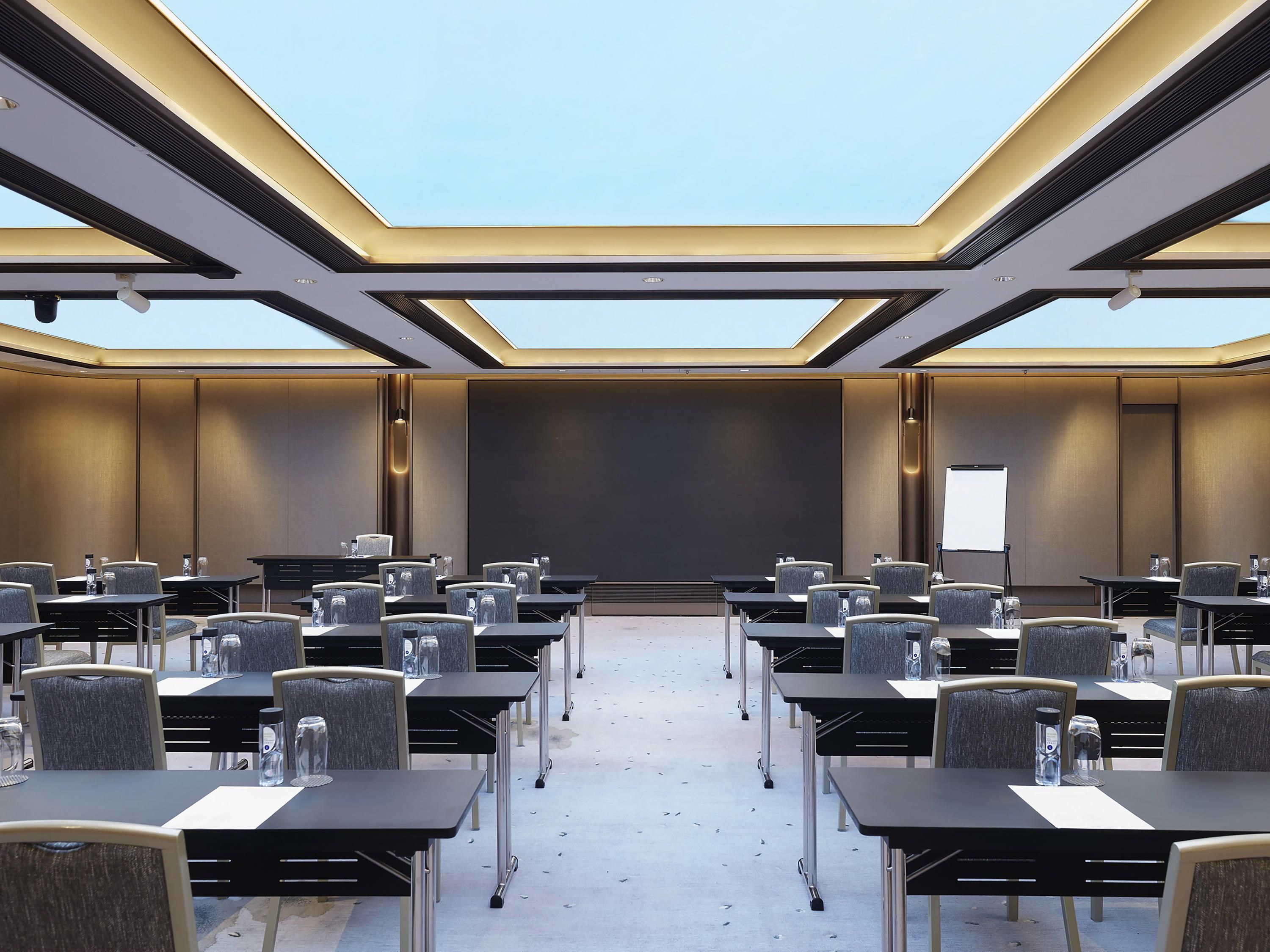 A conference room with tables and chairs, a projector screen, and a skylight.