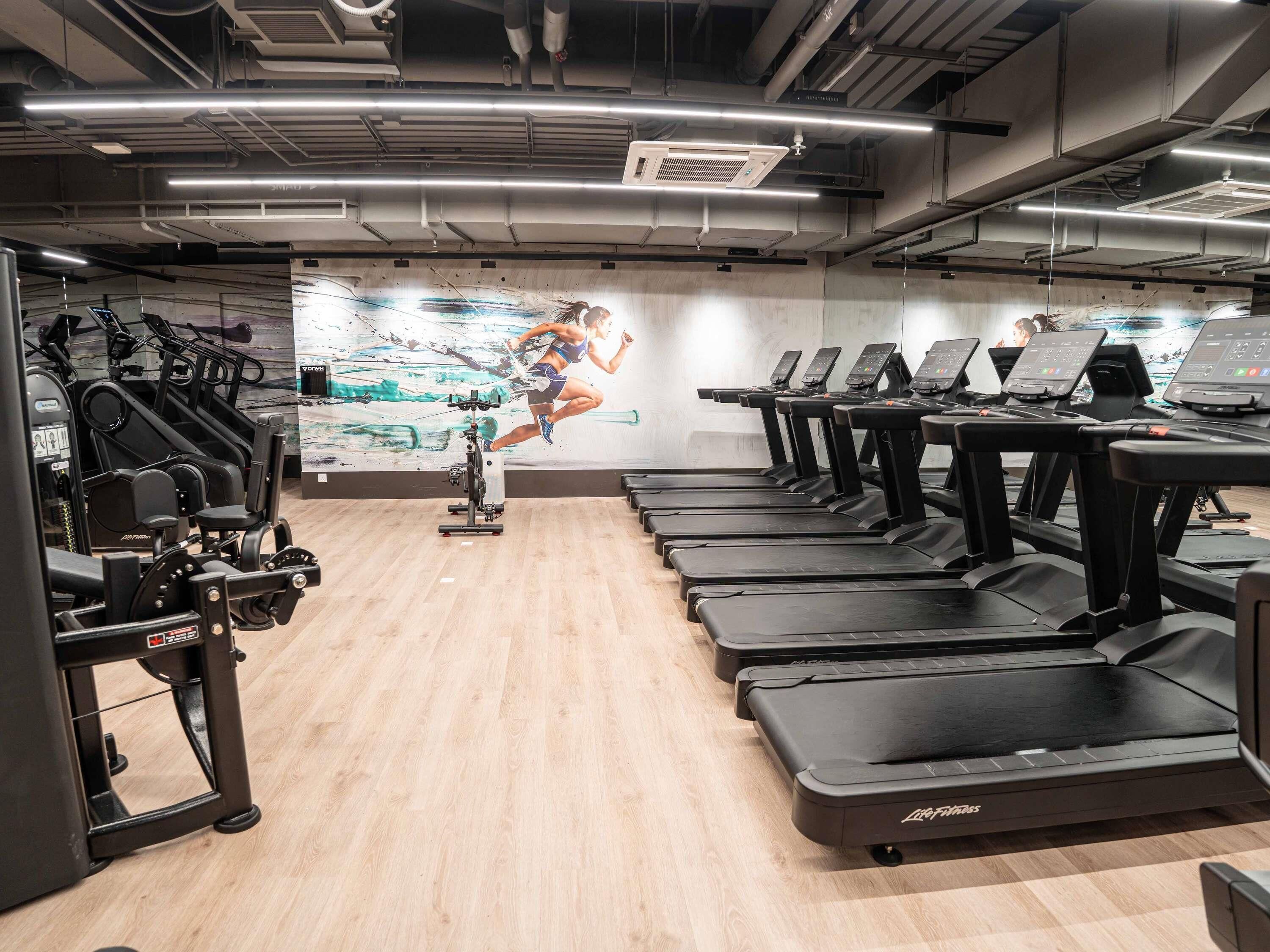 A gym with treadmills, weight machines, and a large mural of a runner.