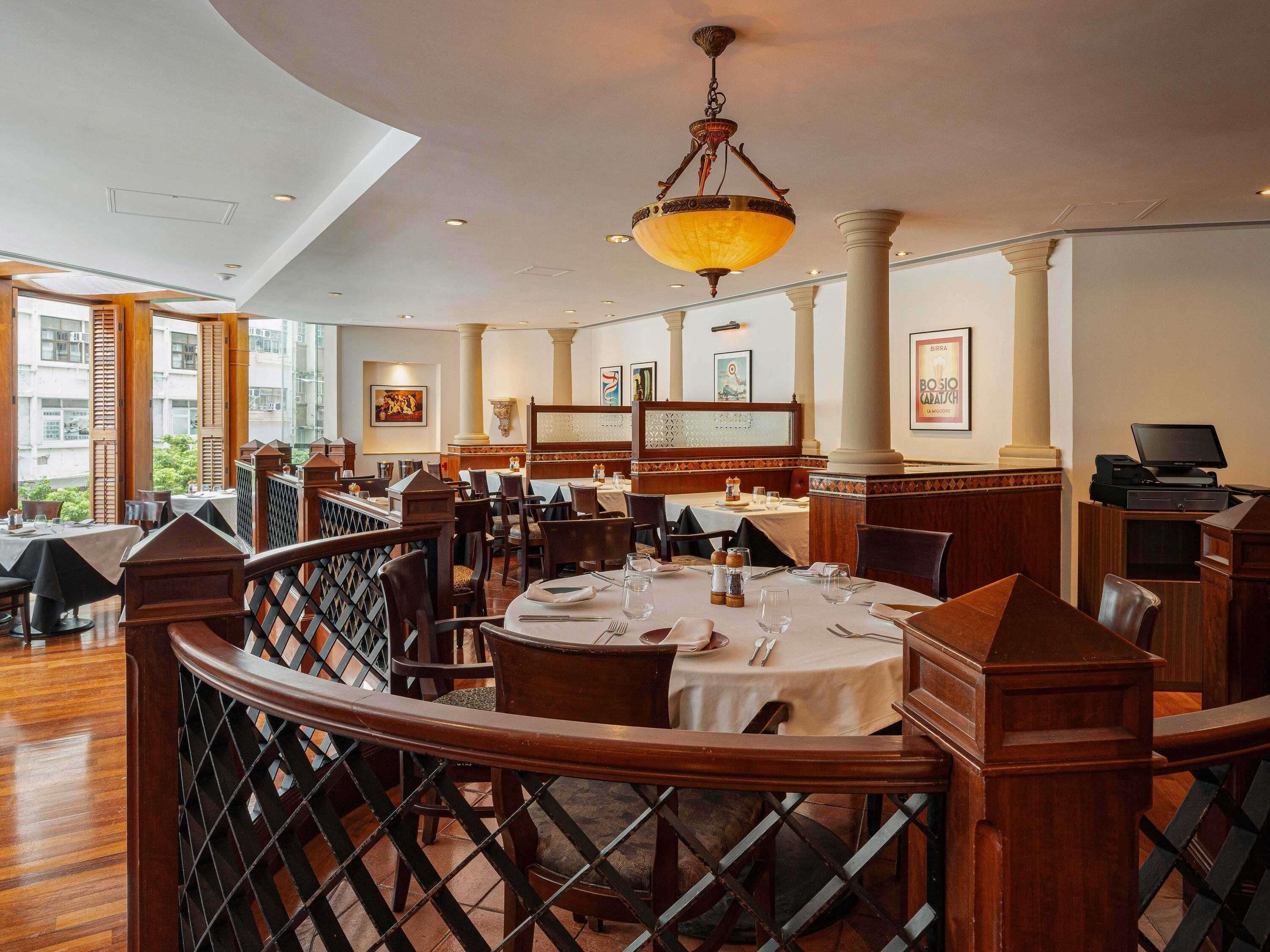 A restaurant with round tables, wooden chairs, and a high ceiling with a hanging light fixture.