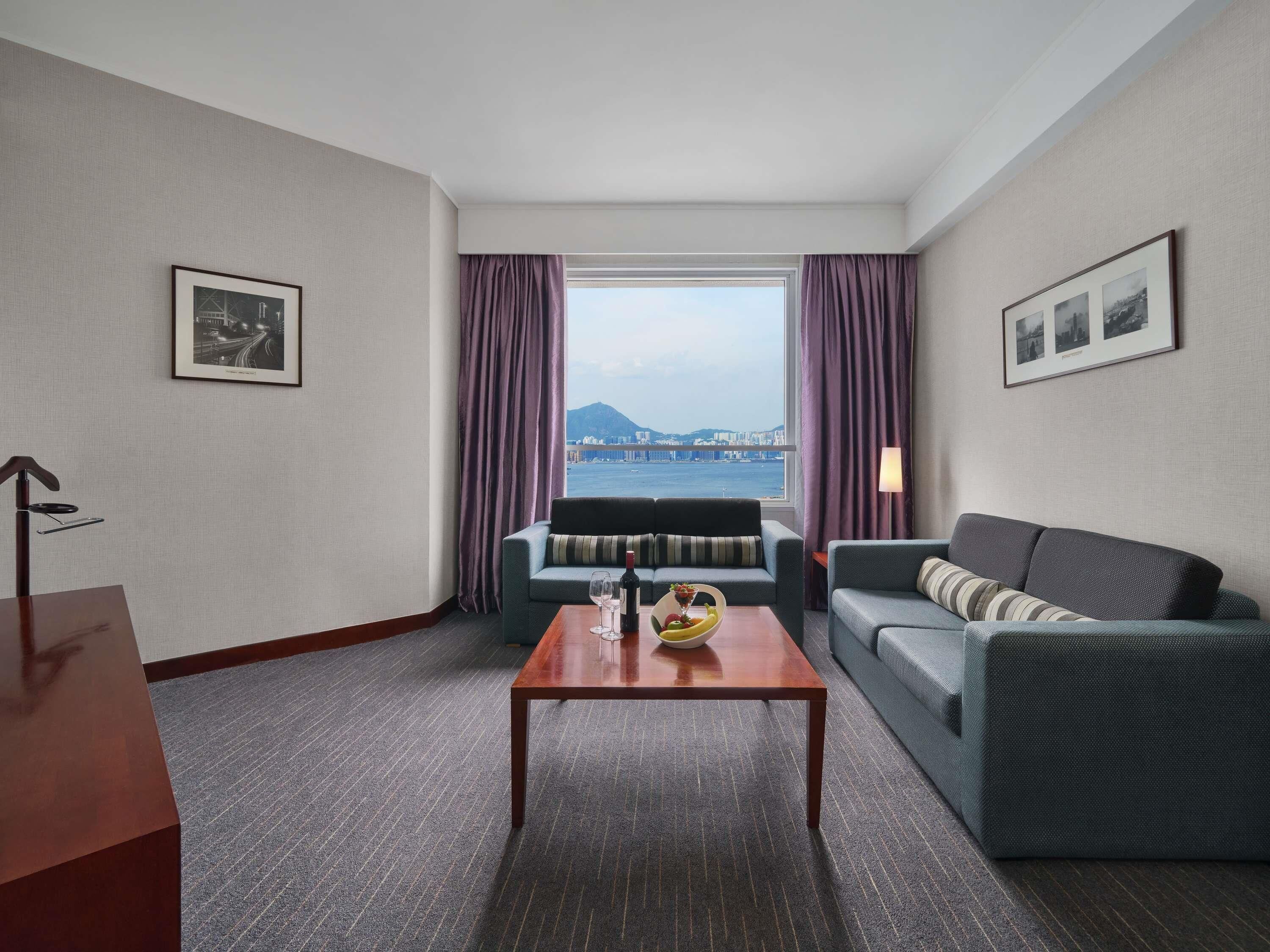 A hotel room with a large window, two sofas, a wooden coffee table, and a lamp.