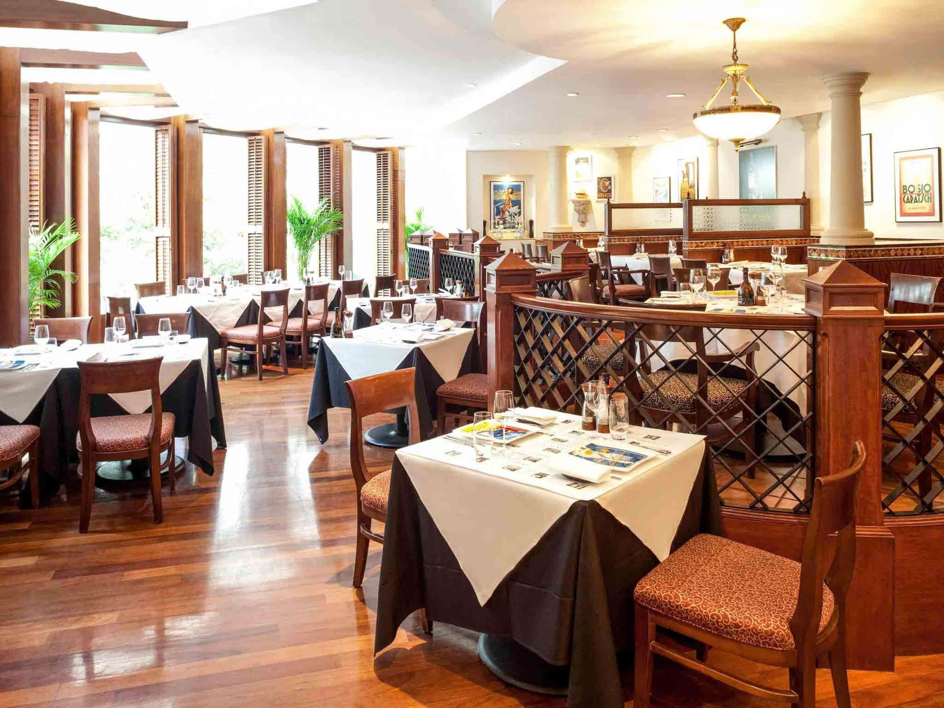 A restaurant with multiple tables and chairs, wooden floors, and a decorative partition.