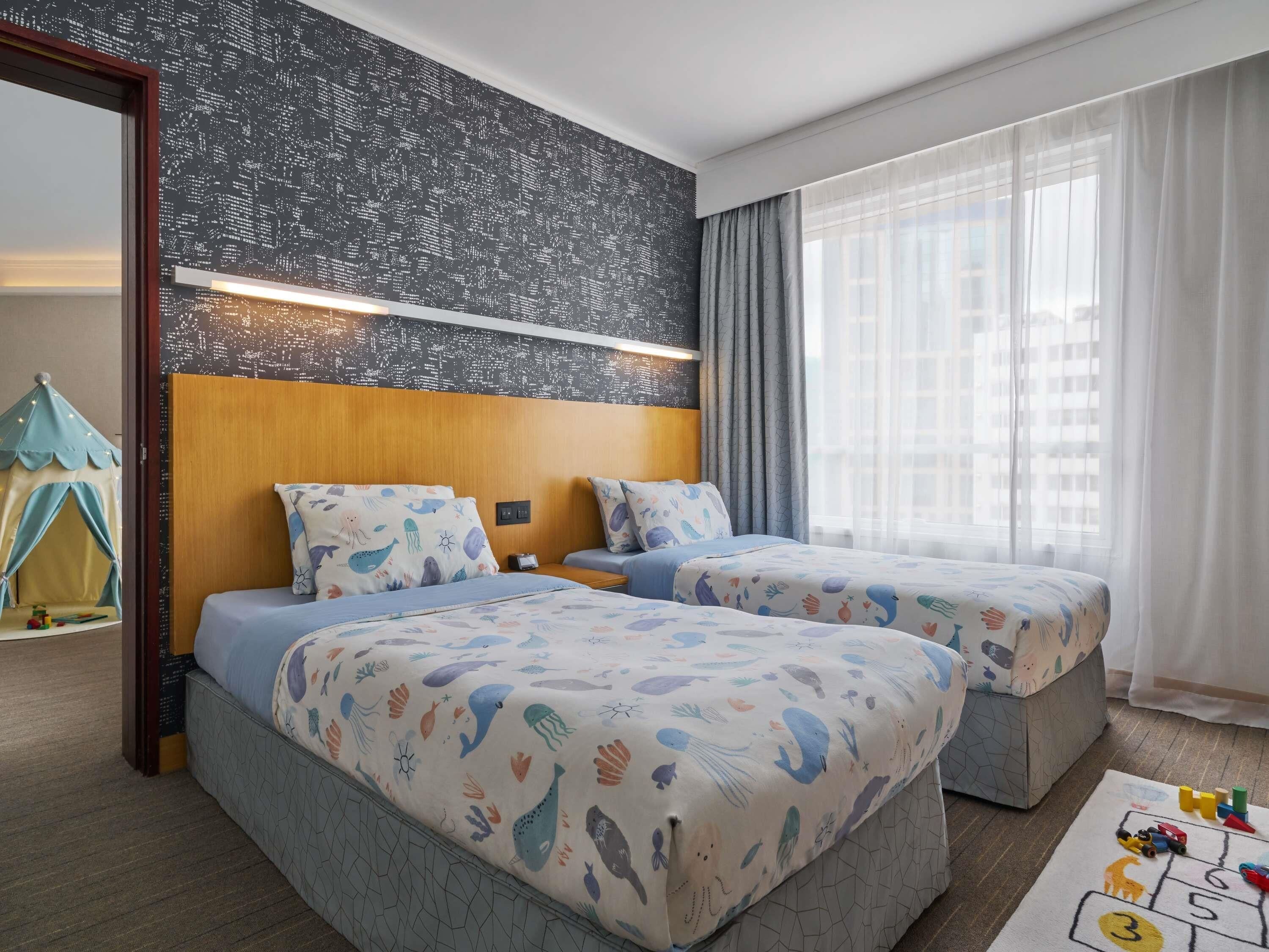 Ein Hotelzimmer mit zwei Betten, einem Spielbereich und Blick auf die Stadtlandschaft.