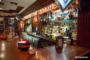 Una zona de bar con un mostrador de madera, estantes llenos de botellas de licores y un televisor montado en la pared.