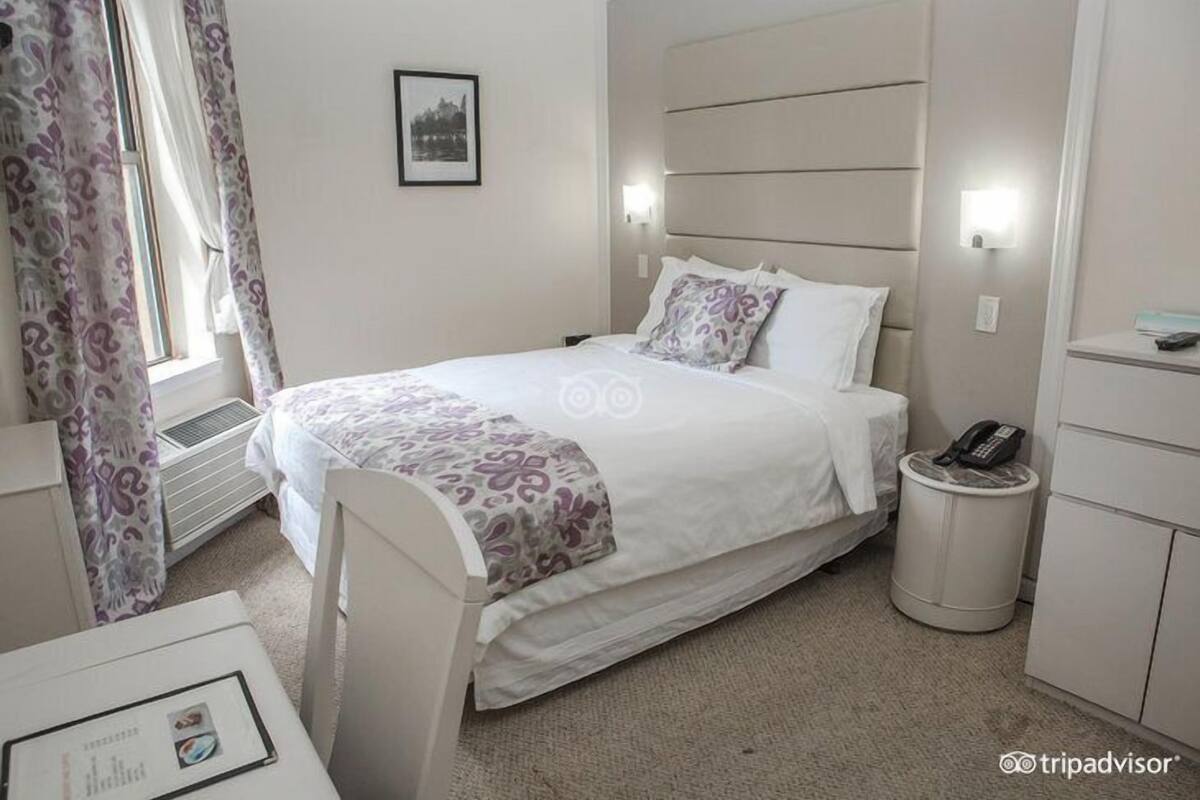 A hotel room with a bed, bedside table, and a trash bin.