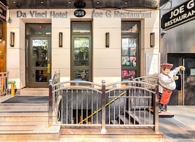 Exterior del hotel Da Vinci y del restaurante Joe G, con una reja metálica y una estatua de chef.