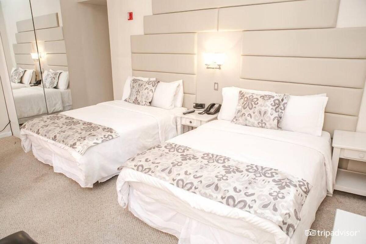 A hotel room with two beds, each with a patterned bedspread, bedside tables with lamps, and a large mirror on one wall.
