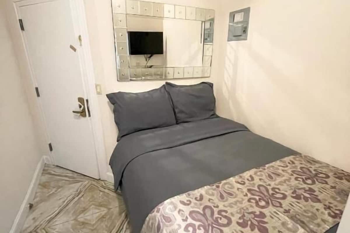 A bedroom with a bed, a door, a wall-mounted TV, and patterned curtains.