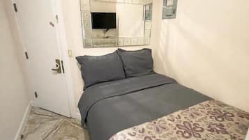 Une chambre à coucher avec un lit, une porte, un téléviseur fixé au mur et des rideaux à motifs.