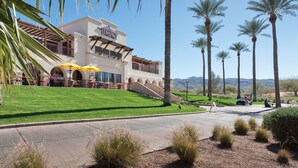 A hotel with a patio area, palm trees, and a view of the mountains.