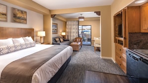 A hotel room with a large bed, a sofa, a desk, a TV, and a kitchen area.