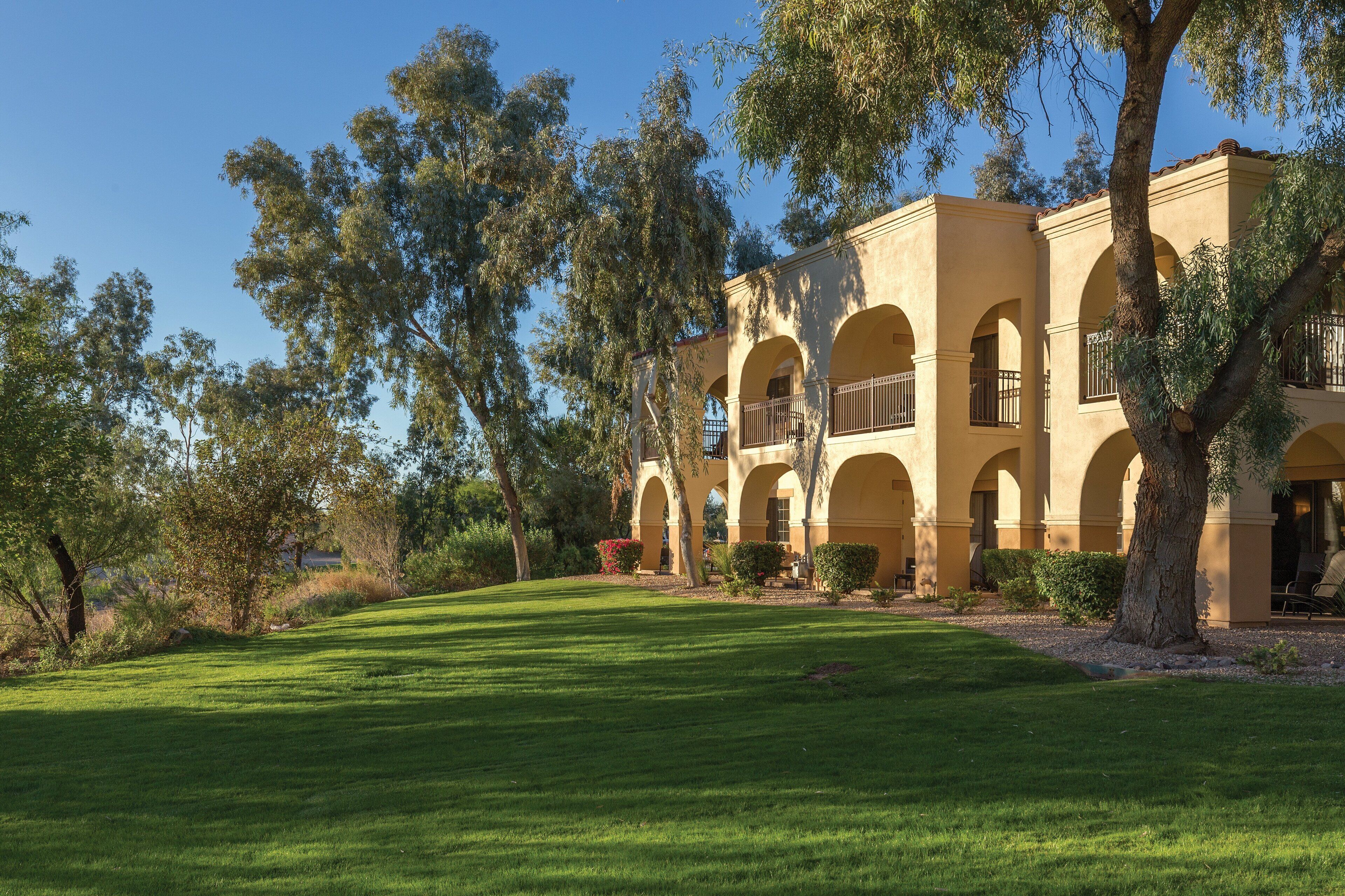 A building with multiple arches and balconies, surrounded by trees and a well-maintained lawn.