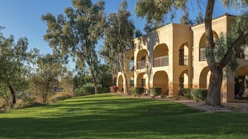 A building with multiple arches and balconies, surrounded by trees and a well-maintained lawn.