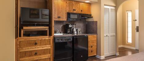 A compact kitchen with wooden cabinets, a microwave, a coffee maker, and a dishwasher.