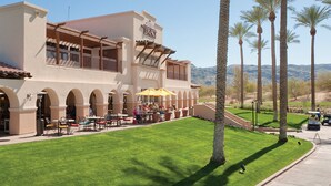 A hotel with outdoor seating, palm trees, and a clear sky.