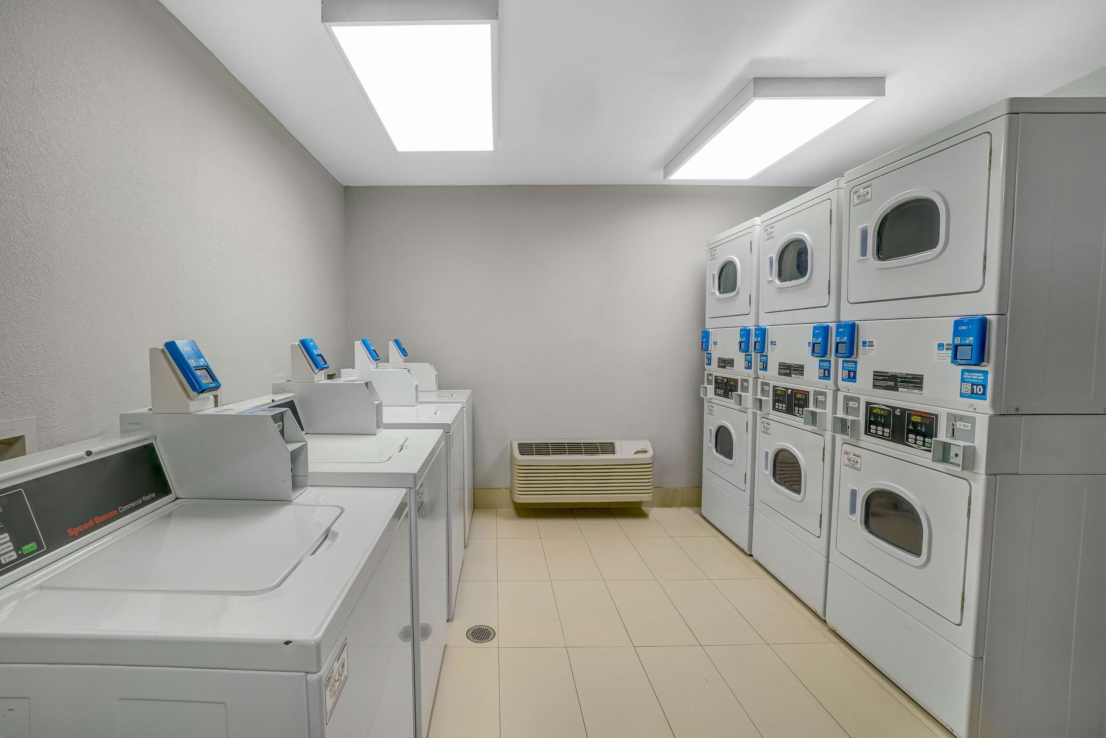 A laundry facility with multiple washing machines and dryers, a ventilation unit, and a control panel.