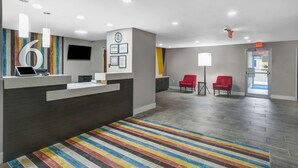 A modern reception area with a large '6' sign, a reception desk, two red chairs, and a colorful striped carpet.