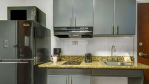 A compact kitchen with a refrigerator, microwave, and built-in oven. It includes a granite countertop, a sink, and cabinets with silver handles.