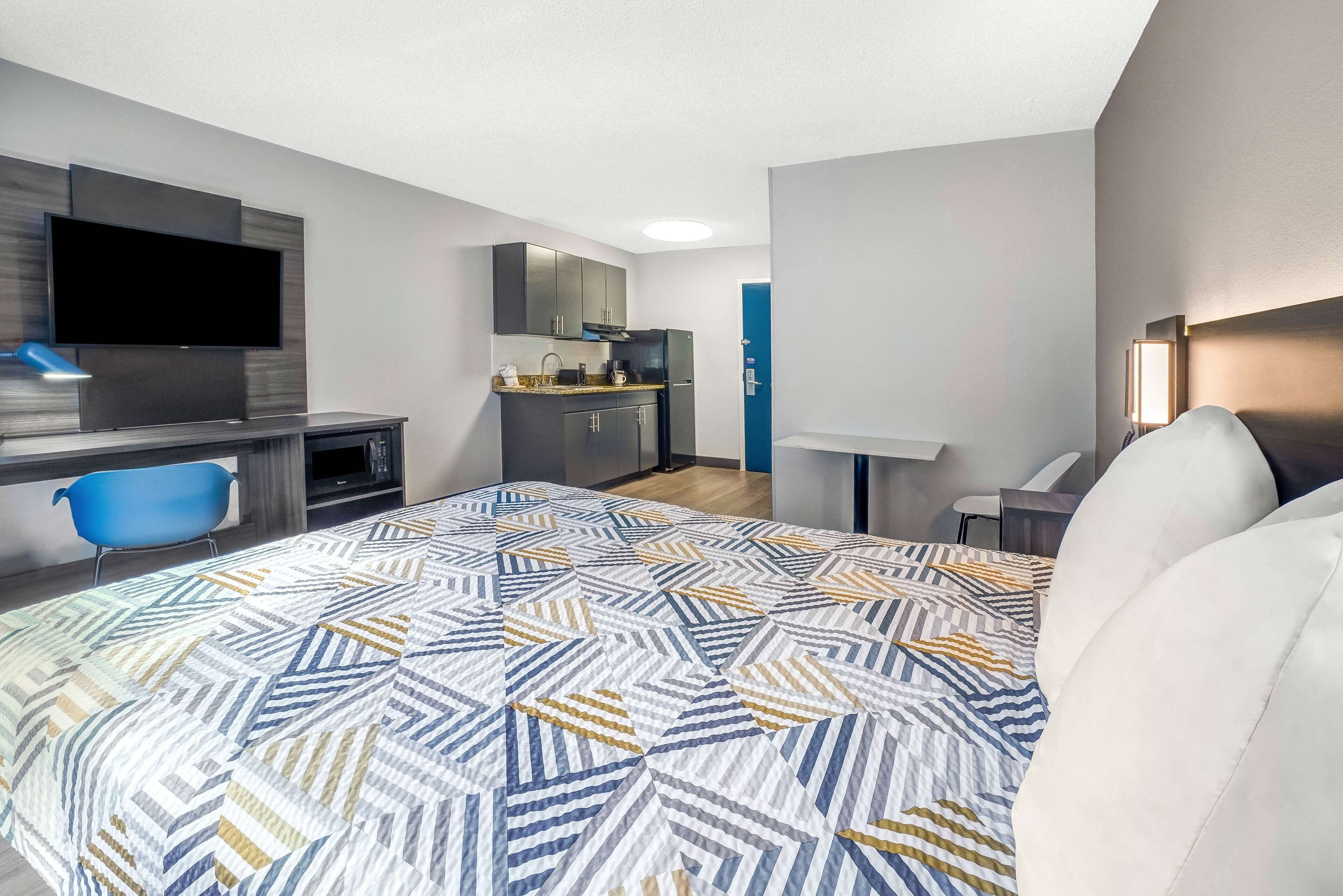 Una habitación de hotel moderna con una cama grande, un escritorio, un televisor, una kitchenette y un baño.
