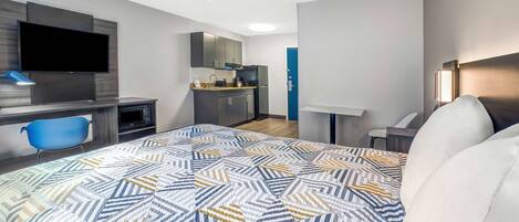 Una habitación de hotel moderna con una cama grande, un escritorio, un televisor, una kitchenette y un baño.