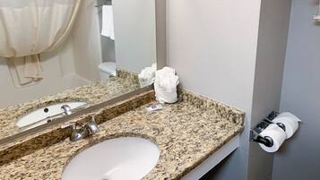 A bathroom with a granite countertop, a sink, a mirror, and a toilet. There are towels and a hand dryer on the counter.