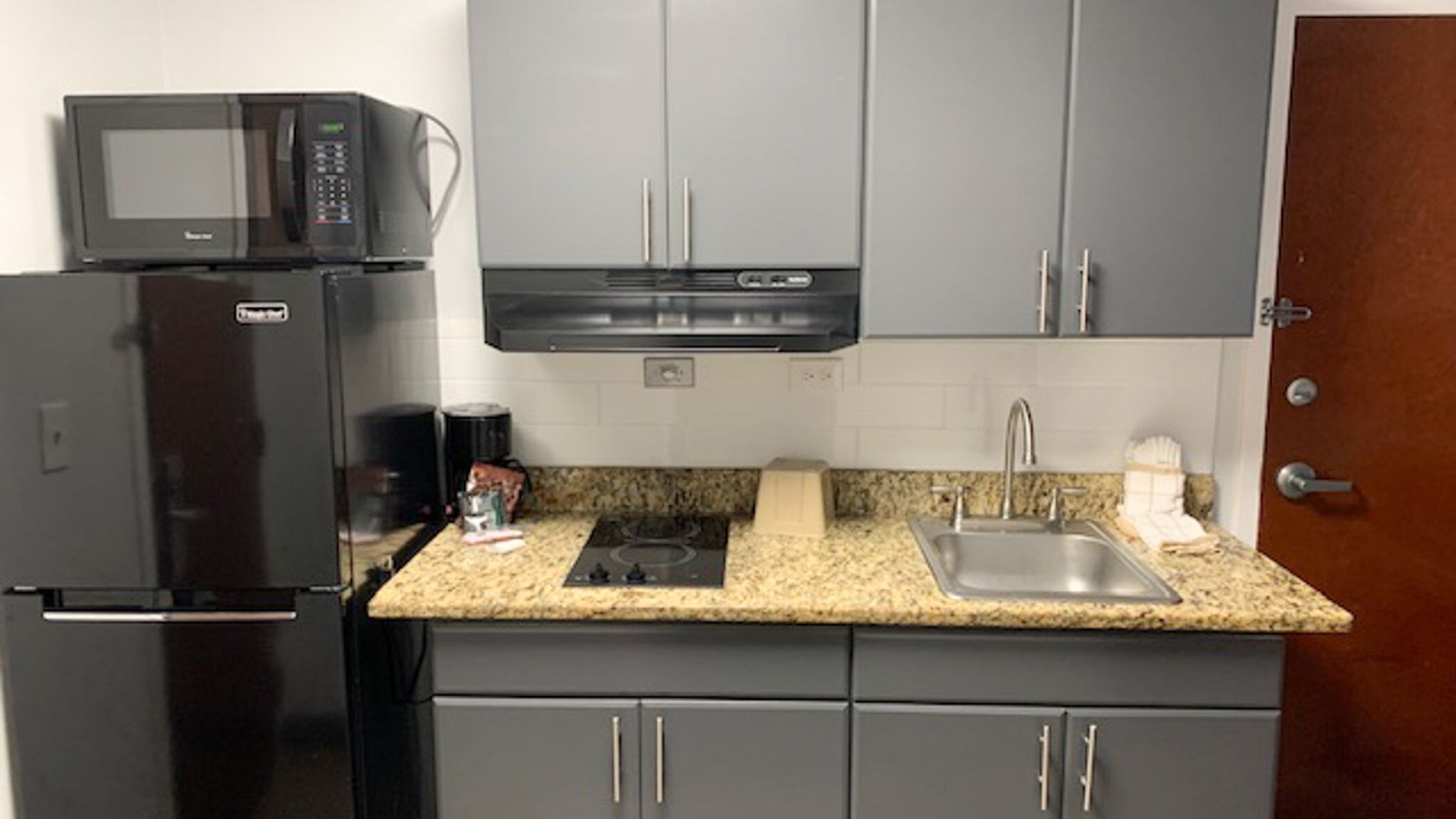 A compact kitchen with a refrigerator, microwave, stove, sink, and cabinets.