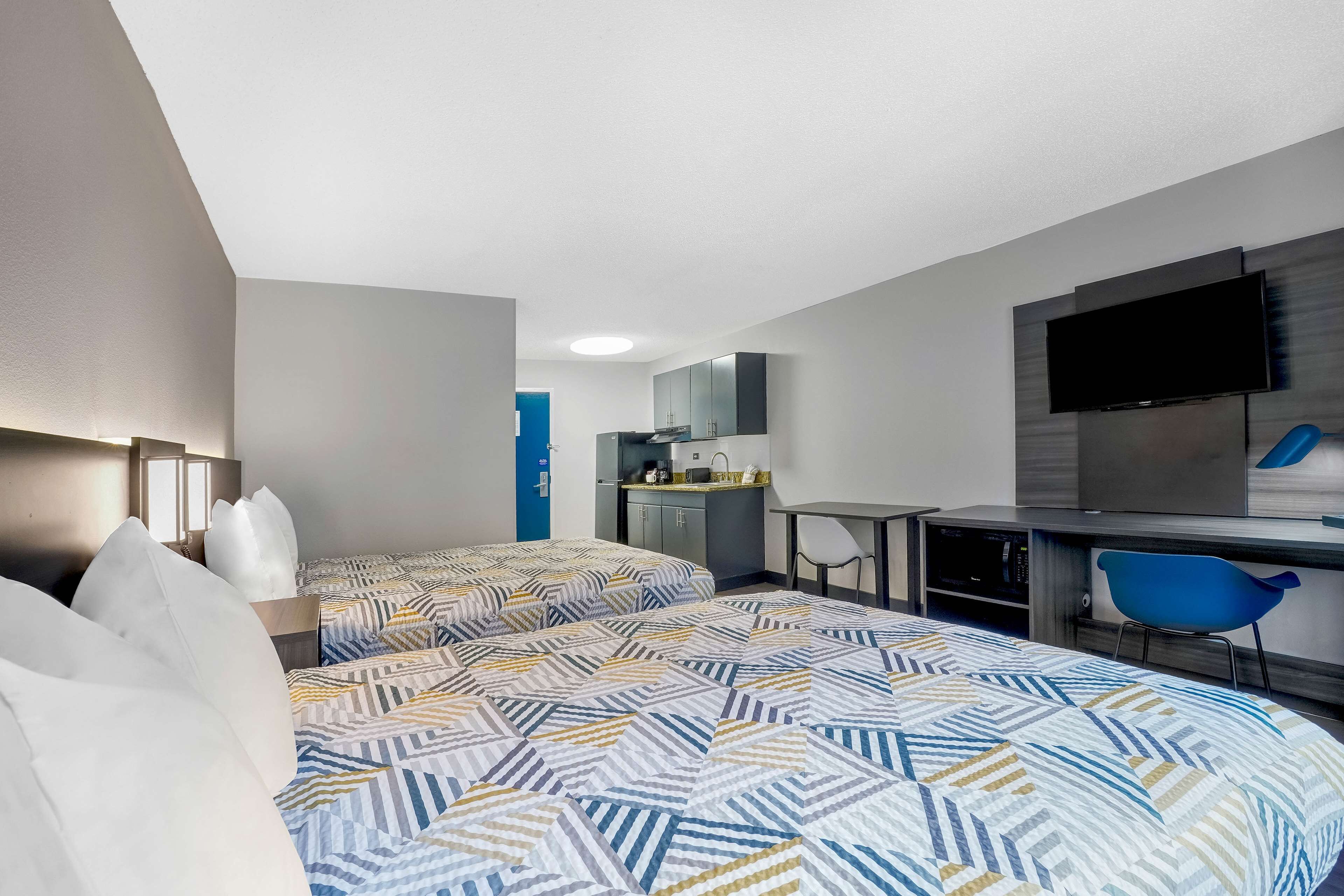 Habitación de hotel con dos camas, un escritorio, una silla, un televisor y una kitchenette.