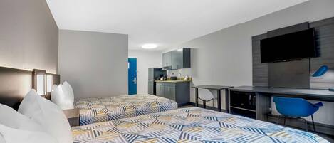 Habitación de hotel con dos camas, un escritorio, una silla, un televisor y una kitchenette.
