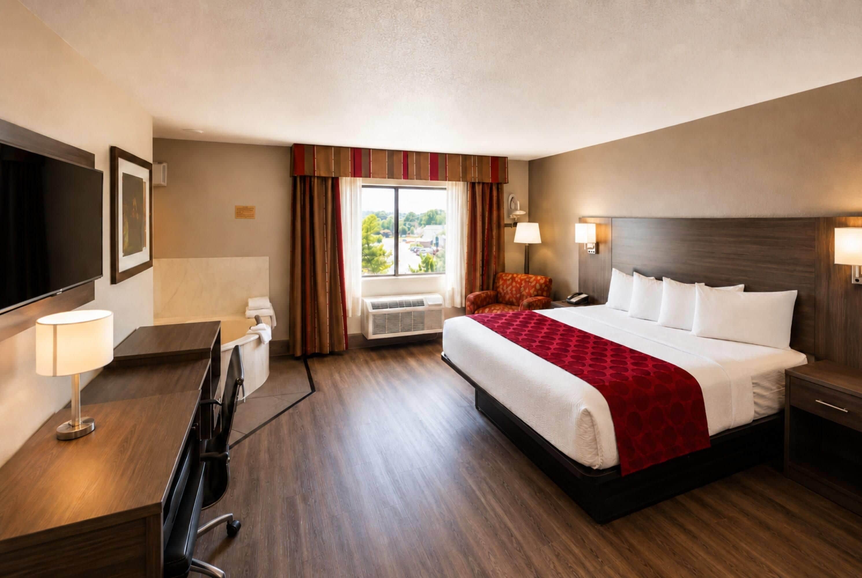 A hotel room with a bed, a desk, a chair, a TV, and a window with curtains.