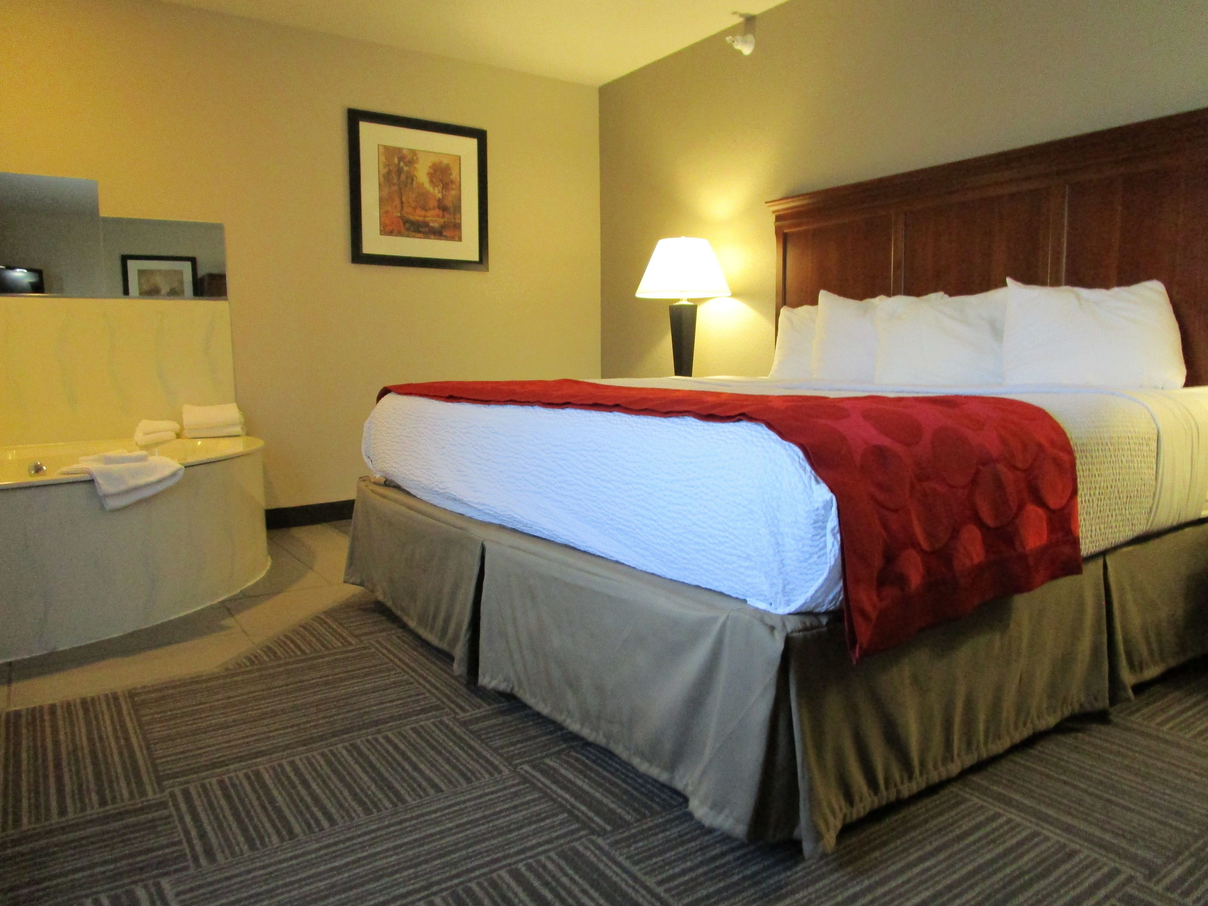 A hotel room with a bed, a desk with a lamp, and a painting on the wall.