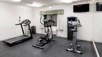 Un gimnasio con caminadora, elíptica y bicicleta estática, un reloj y un televisor en la pared.