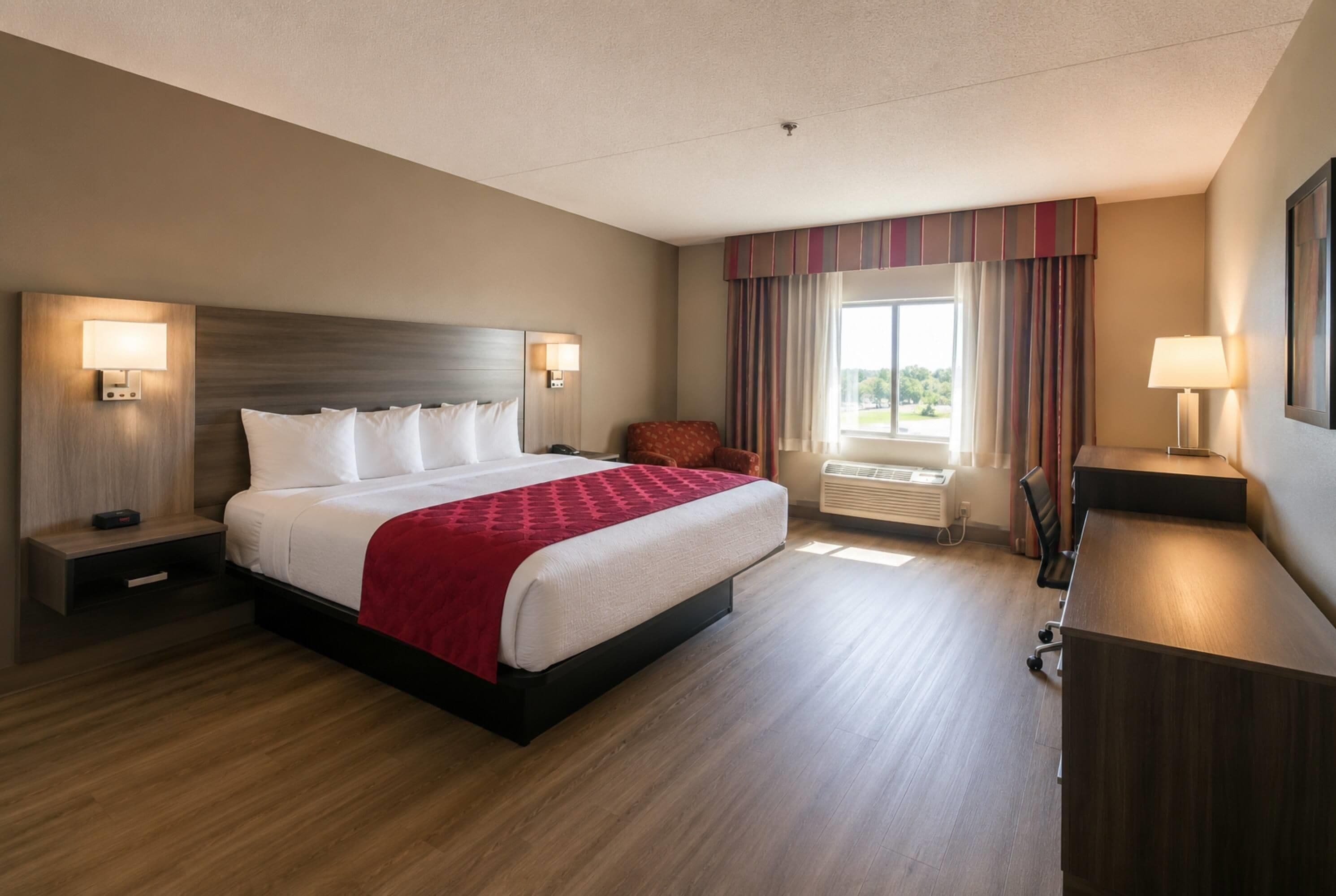 Habitación de hotel con una cama grande, lámparas de noche, un escritorio y una ventana con cortinas.