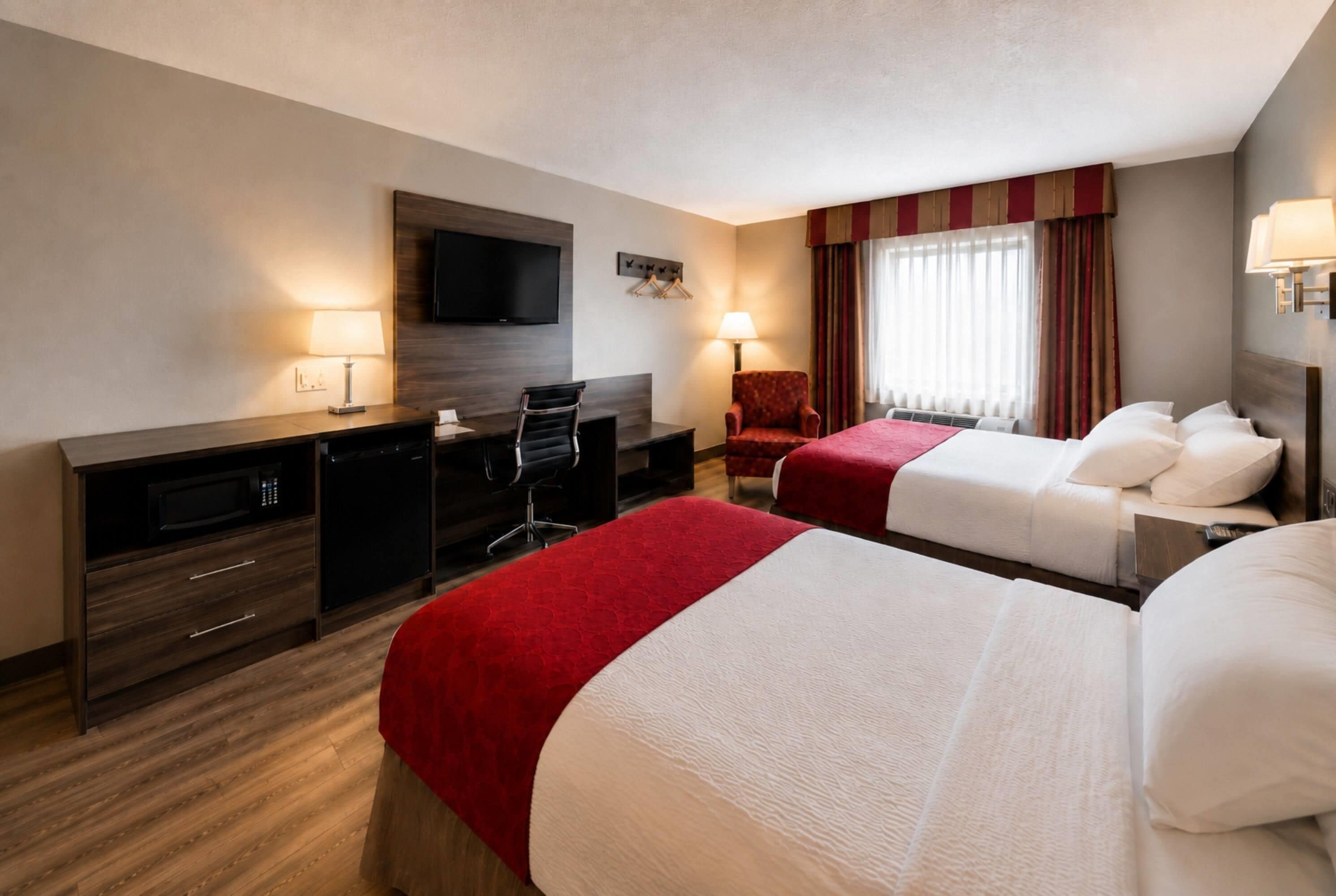 Habitación de hotel con dos camas, un escritorio, una silla, un televisor y una ventana con cortinas.