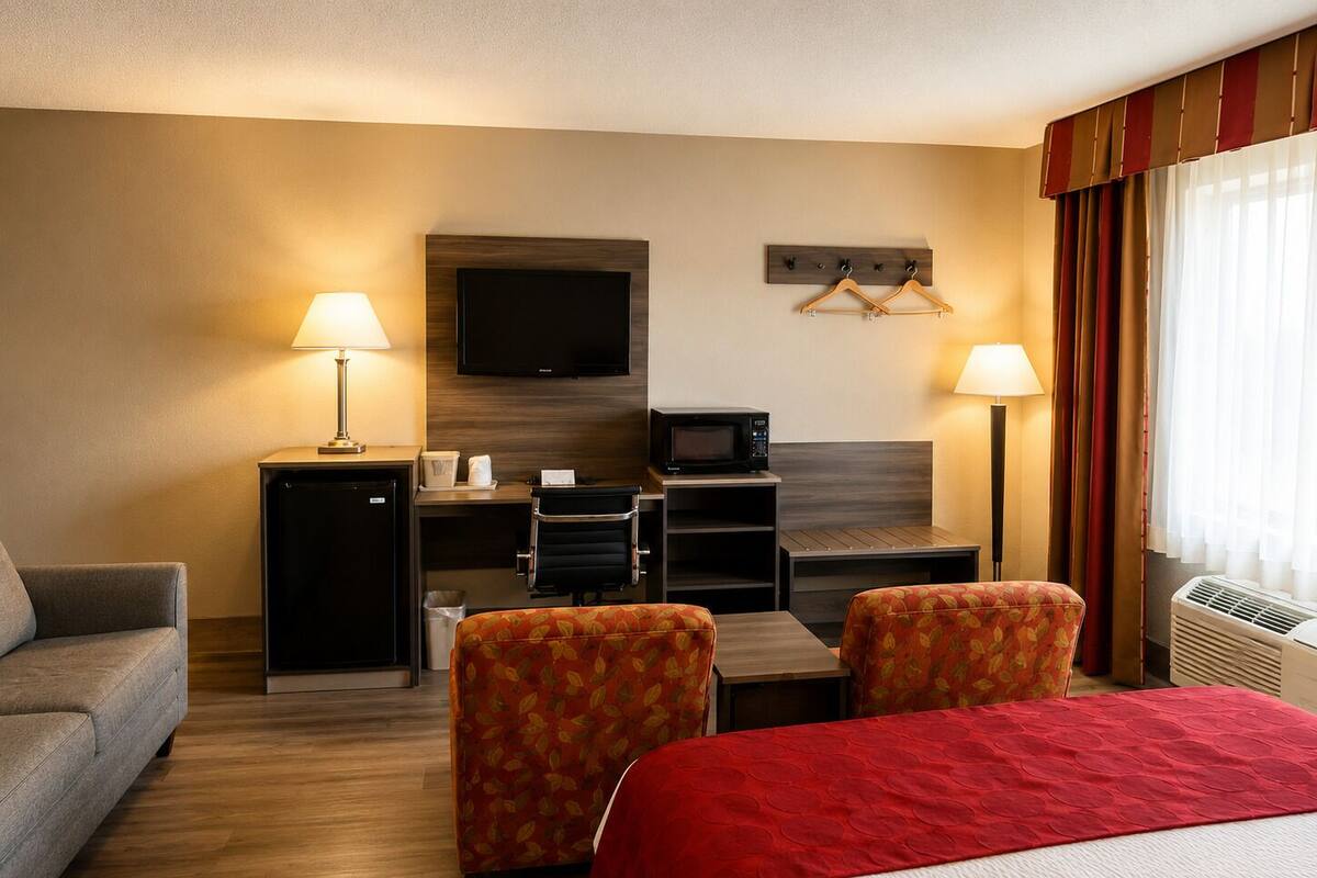 Une chambre d’hôtel comprenant un lit, deux fauteuils, un bureau avec un ordinateur, une télévision, un four à micro-ondes et un radiateur.