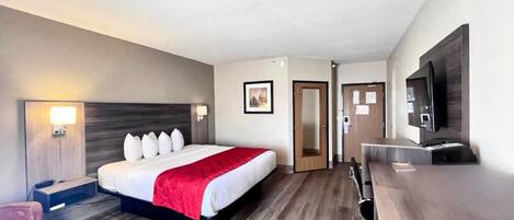 Una habitación de hotel con cama, mesita de noche, lámpara, televisor y escritorio con silla.