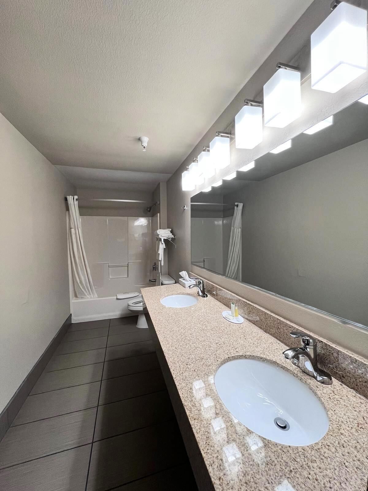 A modern bathroom with two sinks, a large mirror, and a shower area.