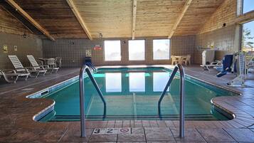 En indendørs swimmingpool med træloft, fliserede vægge og kig til himlen gennem store vinduer.