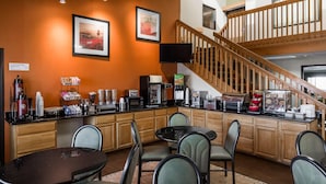 A hotel kitchen with a dining area, a staircase, and a flat-screen TV mounted on the wall.