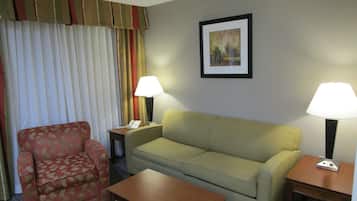Ein Hotelzimmer mit einer Couch, einem Sessel, einem Tisch, zwei Lampen, einem Telefon und einem Bild an der Wand.