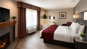 A hotel room with a bed, a TV, a fireplace, a bathroom, and a painting on the wall.