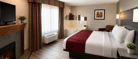 A hotel room with a bed, a TV, a fireplace, a bathroom, and a painting on the wall.