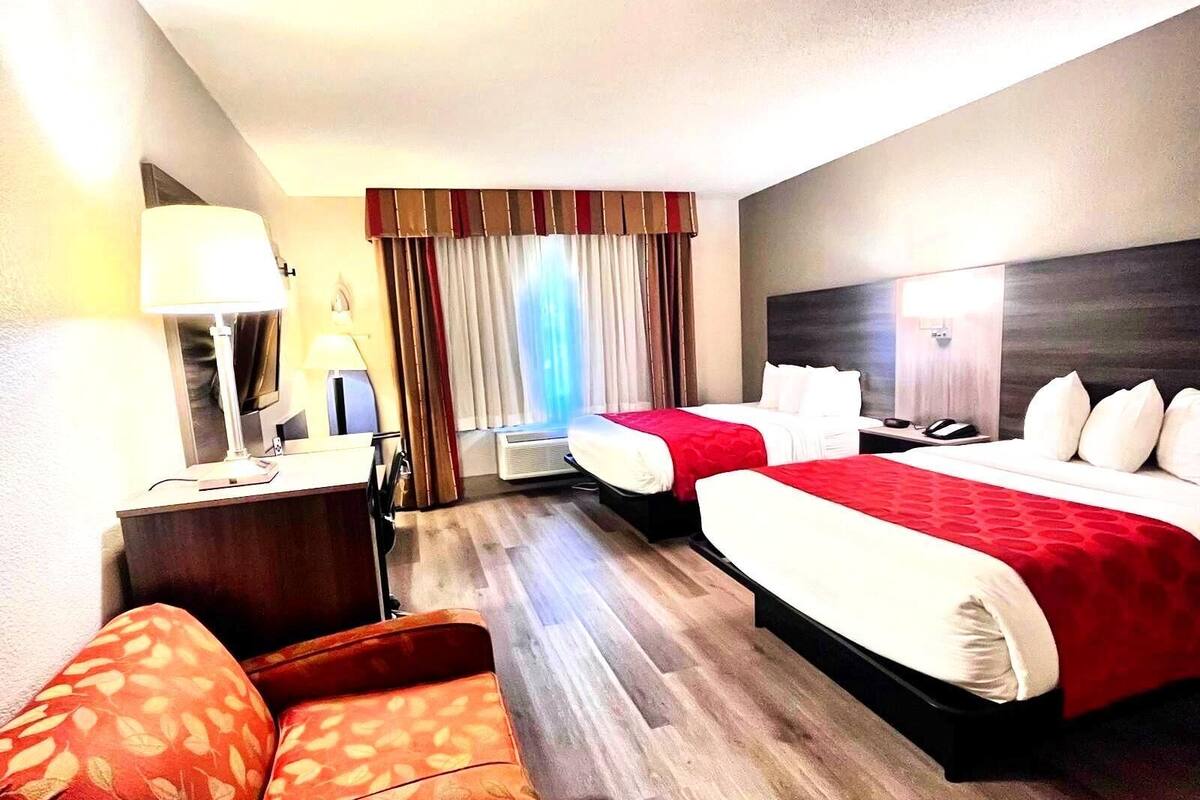 Une chambre d’hôtel avec deux lits, un bureau avec une lampe, une chaise et une fenêtre avec des rideaux.