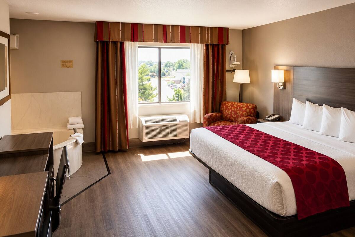Une chambre d’hôtel comprenant un lit, un bureau, une chaise, une fenêtre avec des rideaux et une lampe.