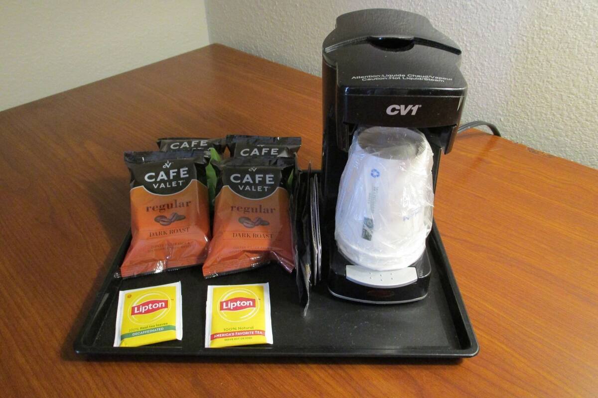 Une machine à café accompagnée de quatre sachets de café torréfié corsé de la marque Cafe Valet et de deux sachets de thé Lipton, le tout présenté sur un plateau.