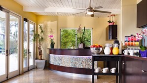A modern kitchen with a central island, a coffee station, and a view of greenery outside. - The Inn at East Beach (Santa Barbara)