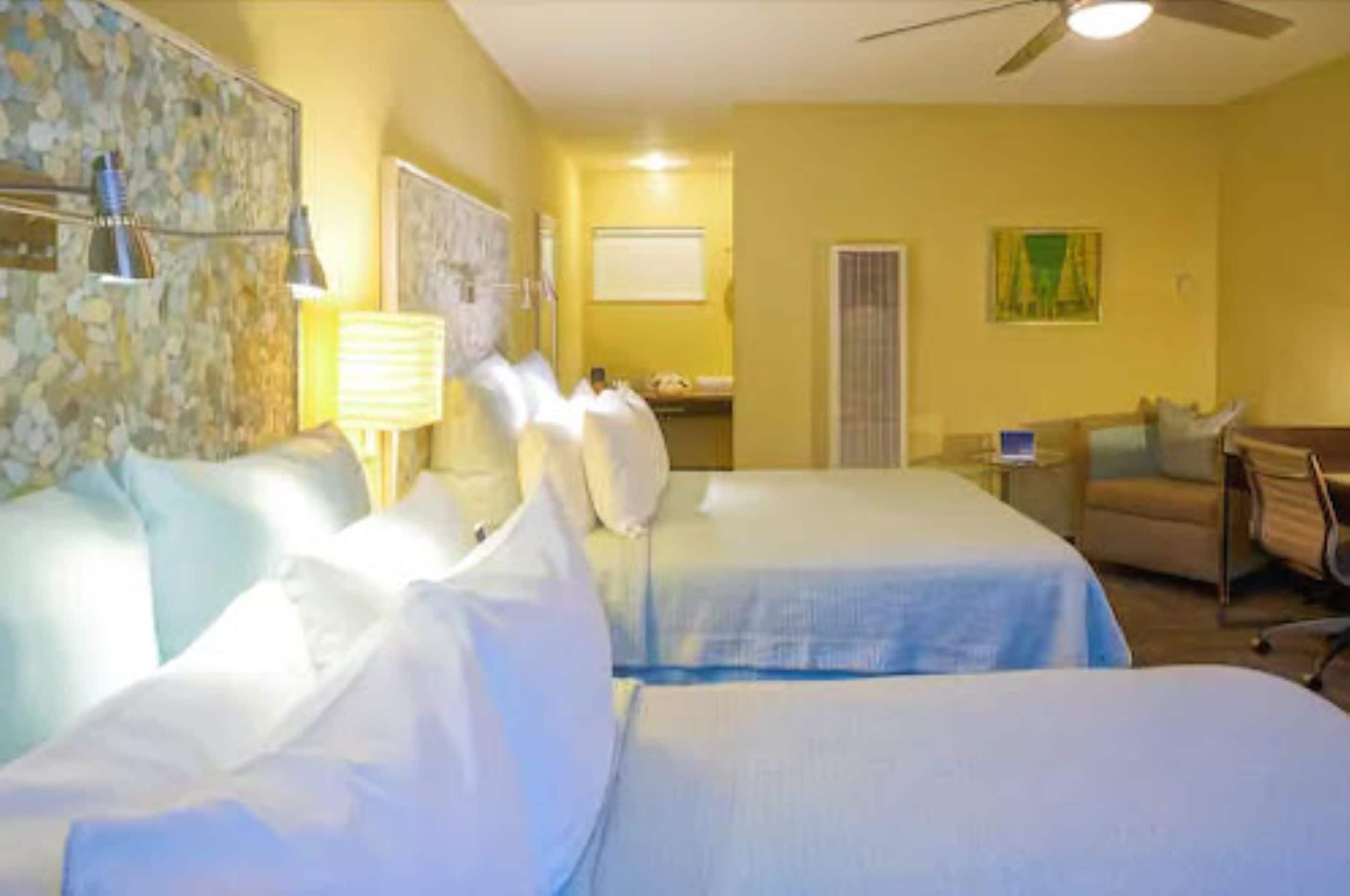 A hotel room with two beds, a desk, a chair, and a ceiling fan.