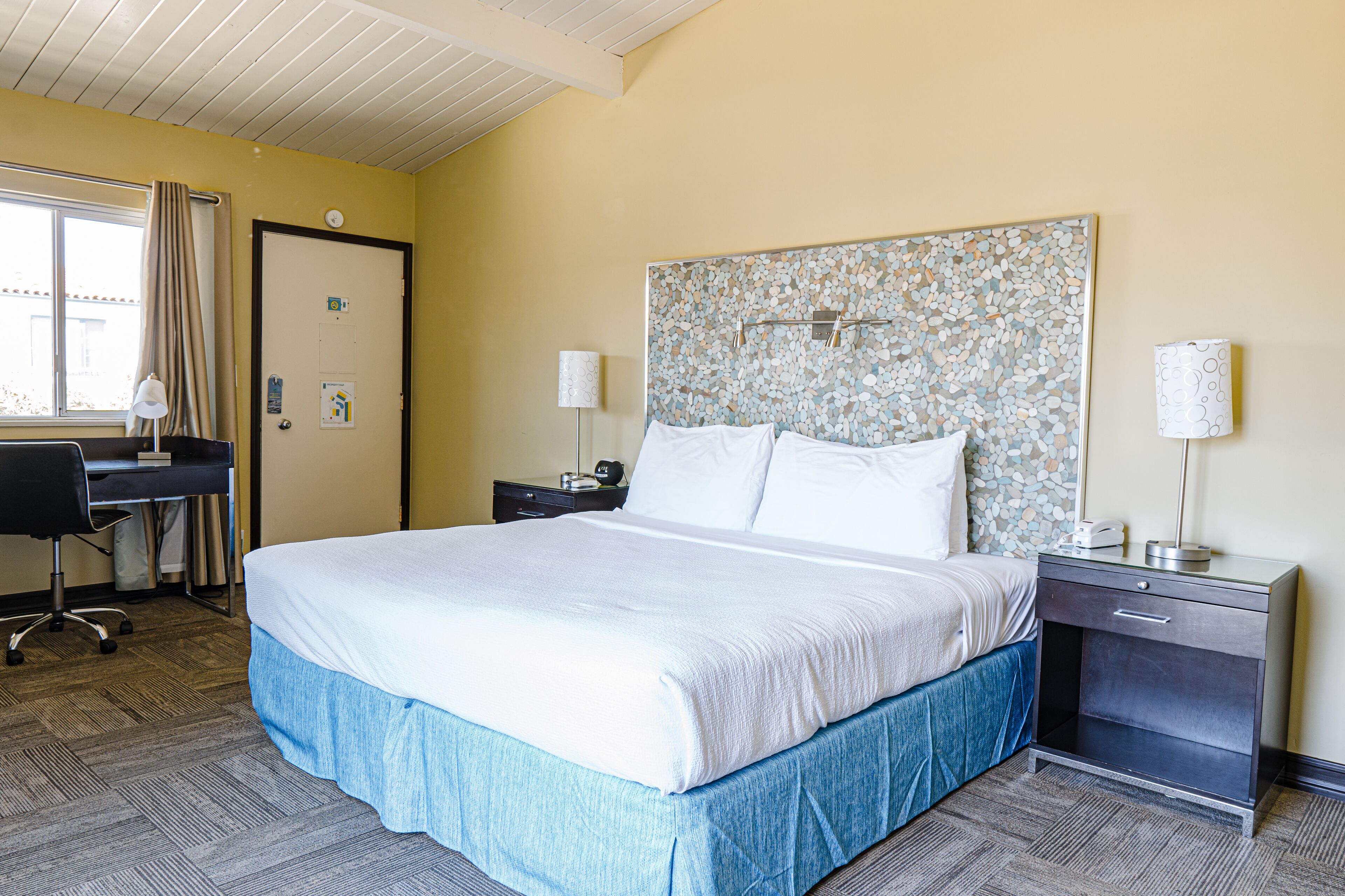 A hotel room with a large bed, a desk, a nightstand, and a lamp.