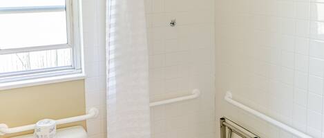 A small, single-bowl toilet with a white tank, a white shower curtain, and a grab bar installed on the wall.
