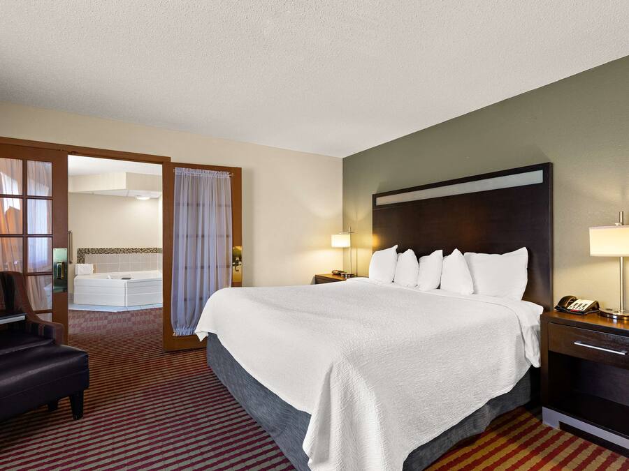 A hotel room with a large bed, a desk with a lamp, a chair, and a bathroom visible through an open door.