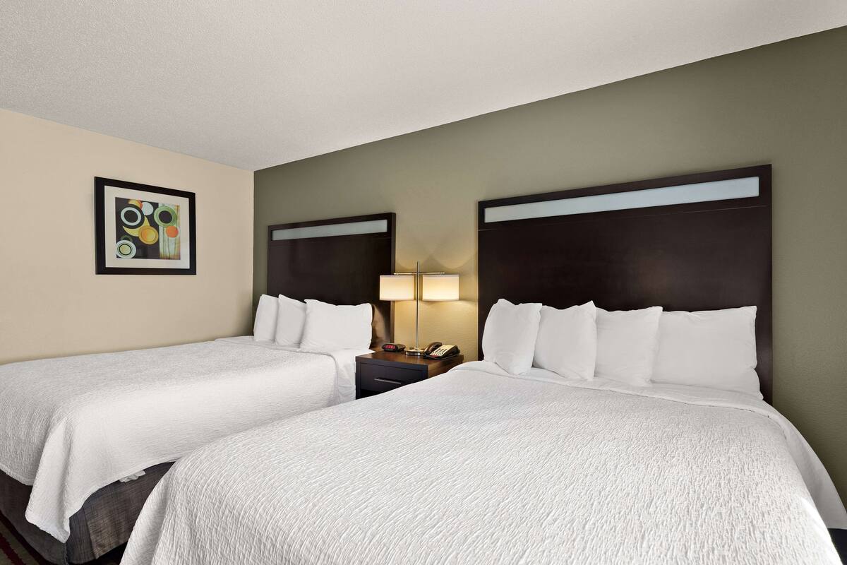 A hotel room with two beds, a nightstand with a lamp, and a framed picture on the wall.