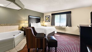 A hotel room with a bed, a desk, a chair, a desk lamp, a TV, a window with curtains, a bathroom with a bathtub, and a tiled wall. - Best Western Germantown Inn (Village of Germantown)